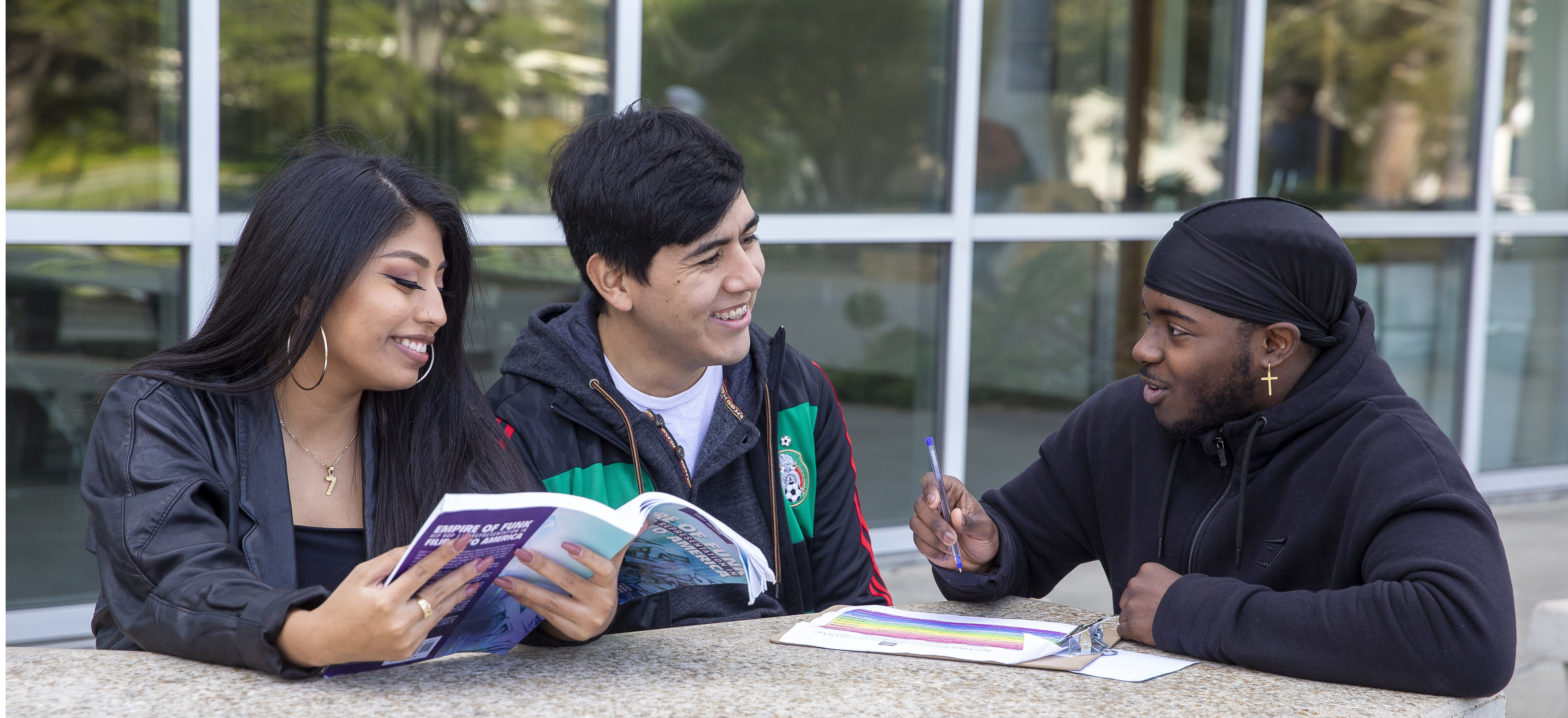 Three students sitting outside the library smiling